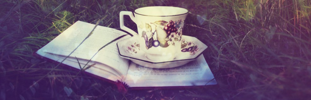 Una tazza di tè con il suo piattino appoggiata su un libro aperto, il tutto in mezzo al verde